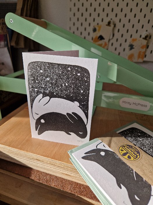 Ein weißer und schwarzer, schlafender, stilisierter Hase unter einem Nachthimmel; gedruckt auf einer weißen Klappkarte