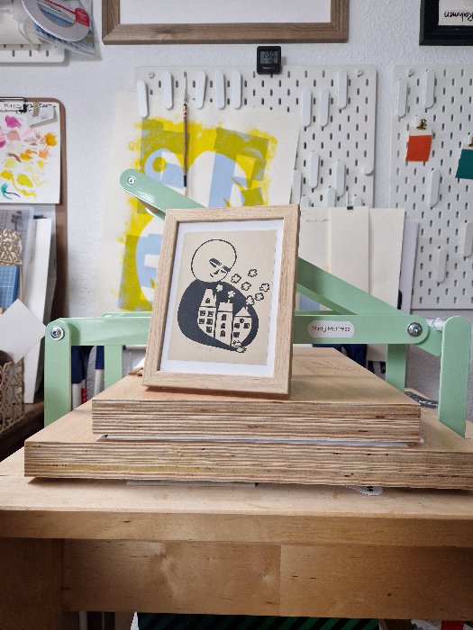 Silisierte lächelnde Person, die mit ihren Armen drei Häuser mit rauchenden Stornsteinen umschließt, in Schwarz gedruckt auf beigem Papier