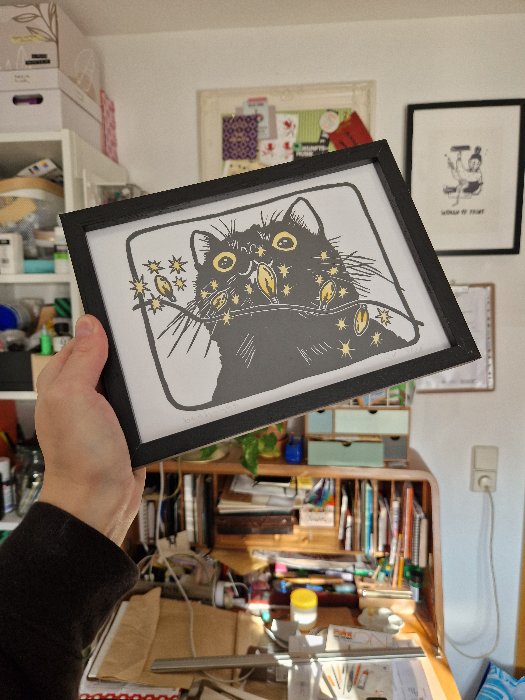 Schwarze Katze, die auf eine Lichterkette mit gelben Glühbirnen starrt; gedruckt auf weißem Papier