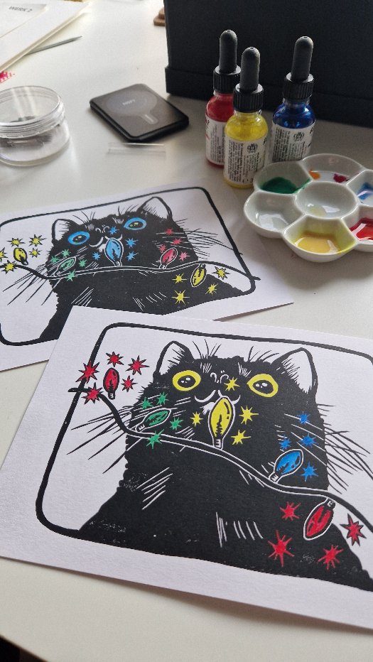 Schwarze Katze, die auf eine Lichterkette mit bunten Glühbirnen starrt; gedruckt auf weißem Papier